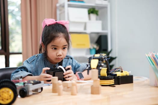 A primary school girl focuses on operating a robotic arm with a remote control, demonstrating STEM education in action.