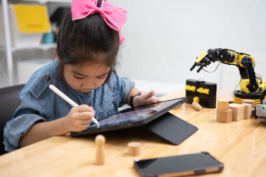 A primary school girl focuses on operating a robotic arm with a remote control, demonstrating STEM education in action.