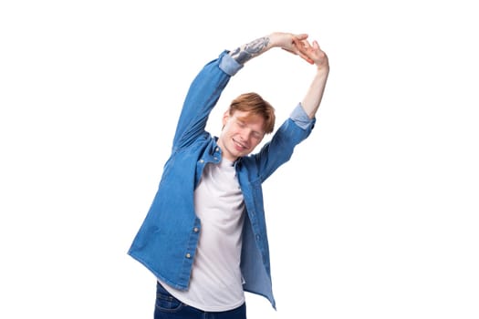 portrait of a smiling caucasian red-haired guy in a denim blue shirt doing exercises.