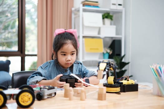 A primary school girl focuses on operating a robotic arm with a remote control, demonstrating STEM education in action.