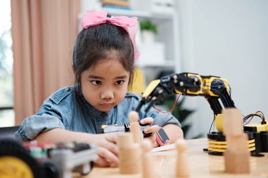 A primary school girl focuses on operating a robotic arm with a remote control, demonstrating STEM education in action.