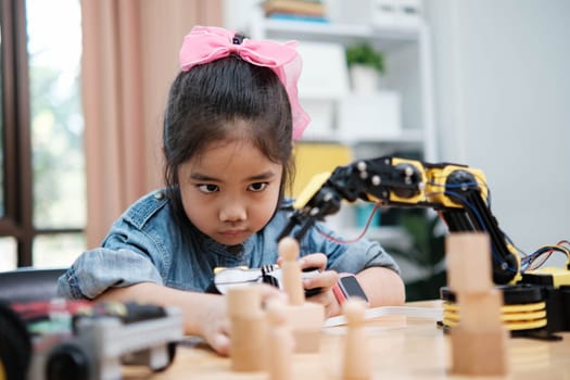 A primary school girl focuses on operating a robotic arm with a remote control, demonstrating STEM education in action.