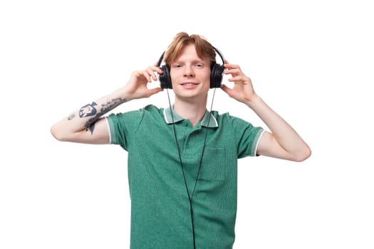 young positive red-haired caucasian guy in a green t-shirt listens to music with headphones.