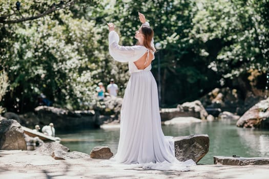 a beautiful woman in a long white dress looks into the distance at a beautiful lake with swans