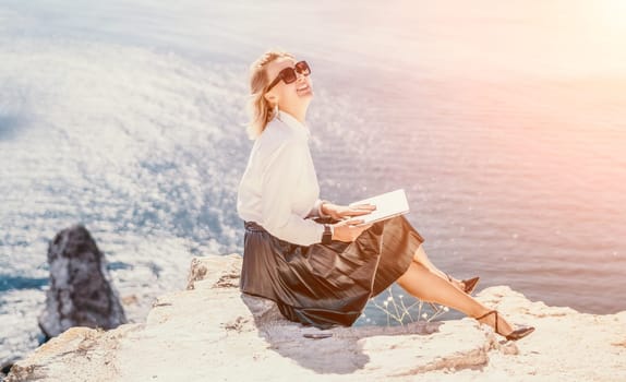 Digital nomad, Business woman working on laptop by the sea. Pretty lady typing on computer by the sea at sunset, makes a business transaction online from a distance. Freelance, remote work on vacation