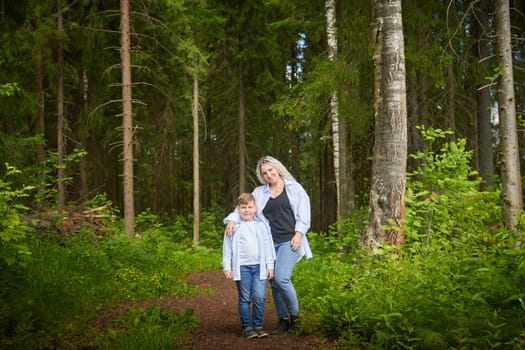 Funny mother with dreadlocks and fat boy happy walking in the forest on a sunny summer day