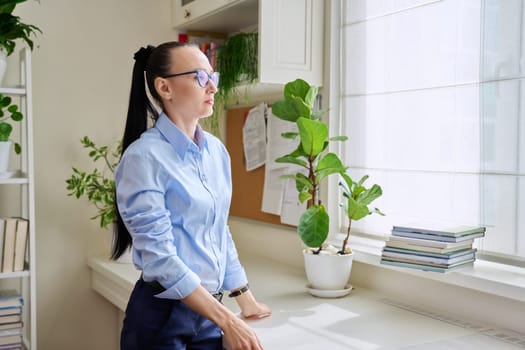 Serious thoughtful woman in her 30s looking out the window. Emotions, lifestyle, health, people concept