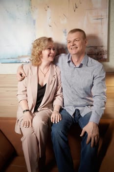 Loving adult couple communicates and embraces privately in the living room or in hotel. Woman is wearing business formal suit and man is wearing jeans and a shirt, indicating a close relationship