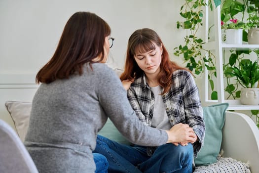 Upset sad mother and daughter teenager sitting together on the couch at home. Family, communication, motherhood, friendship, relationship between parent and teen daughter concept