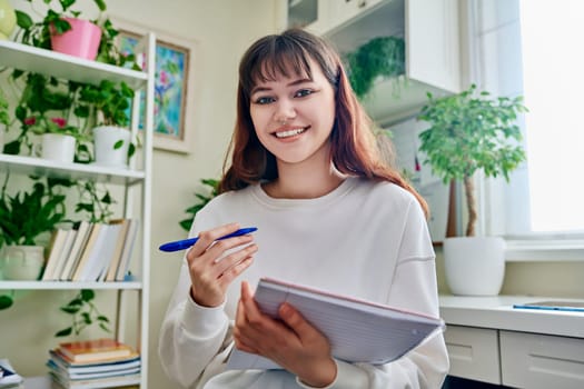 Web camera view of teenage student girl with notebook looking at camera at home. Online lesson video chat call conference. Technology education training e-learning concept