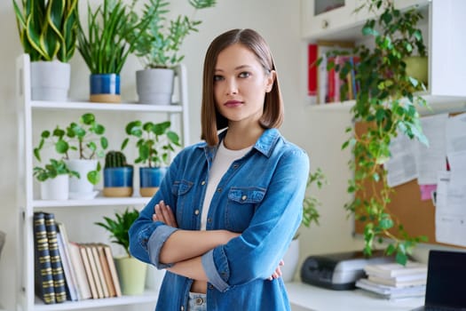 Portrait of young confident smiling woman in home interior. Beautiful positive 20s female with crossed arms looking at camera. Beauty, youth, happiness, health, lifestyle concept