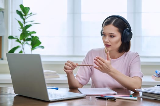 Young female college university student in headphones talking studying using laptop computer for video chat conference call sitting at home. Internet online remote lessons webinars education training