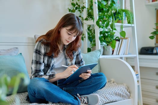 Young female teenager with digital tablet, stylus drawing illustrating sitting on couch at home. Technologies, leisure, creativity, education, freelance work, lifestyle, youth concept