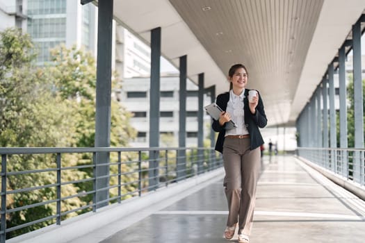 Young busy successful Asian business woman, professional businesswoman holding laptop and using mobile standing or walking on urban business center.