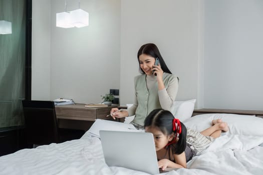 Work from home, freelance and lifestyle concept. Portrait of creative asian female sitting on bed with laptop and her take care of her kid while working.