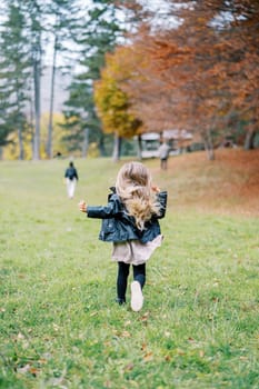 Little girl with flying hair runs along the edge of the autumn forest after her mother. Back view. High quality photo
