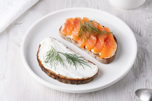 Rye sandwich with salmon and cream cheese on white wooden table.