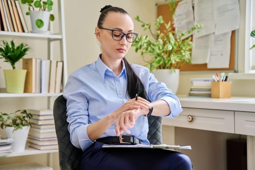 Female psychologist looking at watch on hand sitting at workplace in office. Professional mental therapist counselor psychologist social worker. Health care service psychology psychotherapy treatment