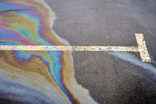 Oil spill on a wet asphalt surface, with a parking lot marked by dividing lines. Addressing environmental concerns about water pollution