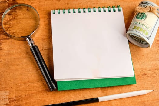 A concept image with banknotes, a notebook with a place to write and a magnifying glass