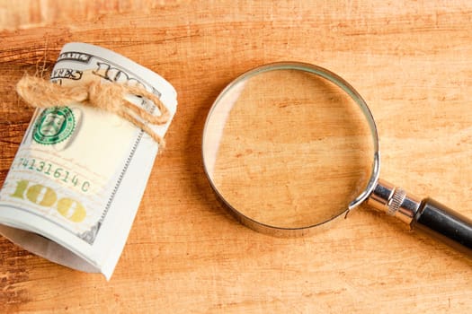 A magnifying glass lying near a roll of bills on a papyrus background. A place to copy