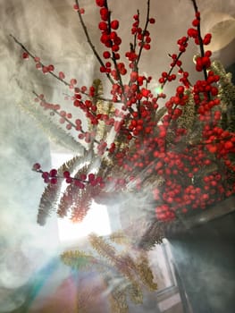 a bouquet of branches with red berries and fir branches in smoke in sunny weather, the rays of the sun through the branches. High quality photo
