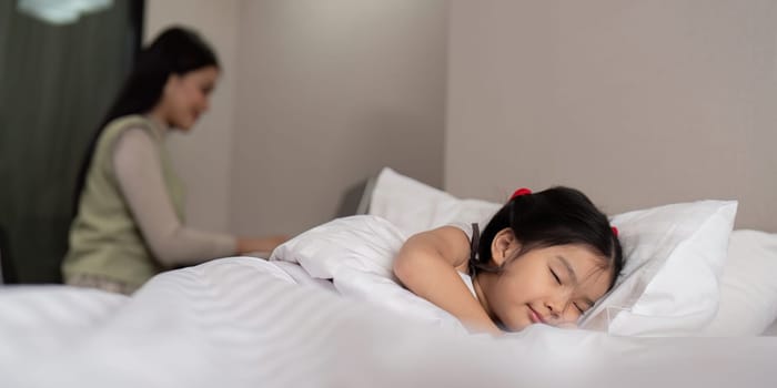 Asian mother working on bed with sleeping daughter by side at home.