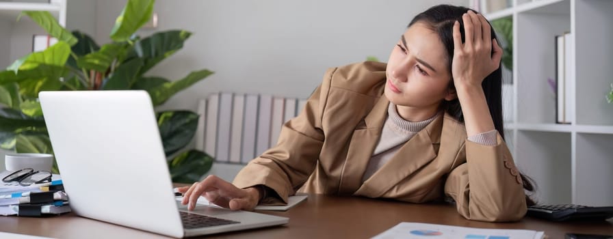 Asian businesswoman feeling tired and stressed over an unsuccessful business while working in a home office decorated with soothing green plants..