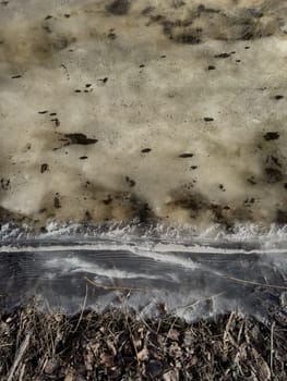 thin transparent ice on a puddle in the park on a spring day, foliage through the ice, dry grass through ice. High quality photo