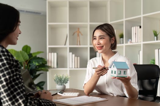 Home sale and home insurance concept, real estate agent with house model talking to client about buy home insurance and client signing contract under formal contract agreement.
