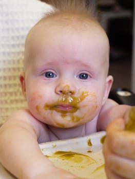 Mom feeding little boy with broccoli puree. Child at the age of six months eats broccoli while sitting on a baby chair.