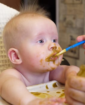 Mom feeding little boy with broccoli puree. Child at the age of six months eats broccoli while sitting on a baby chair.