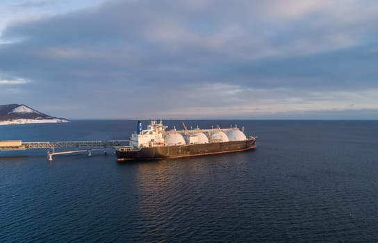 Aerial of Liquified Natural Gas LNG carrier moored to a small gas terminal. Fuel crisis. Sanctions. Wide panoramic shot.