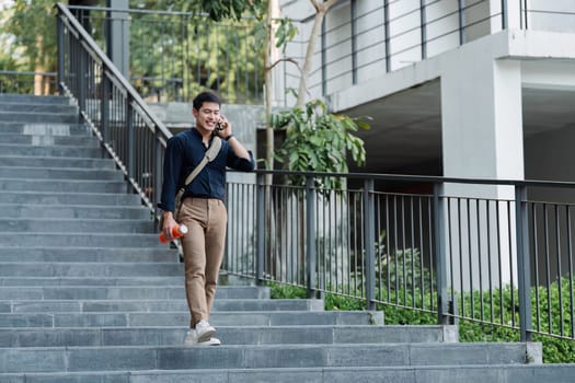 Young business professional walking at business center using mobile and carry bag.