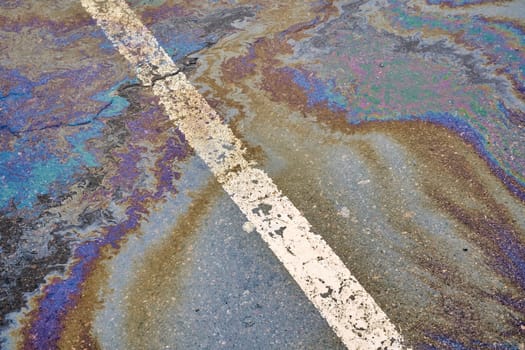 Oil spill on wet asphalt, parking lot with dividing line. Environmental problems of water pollution