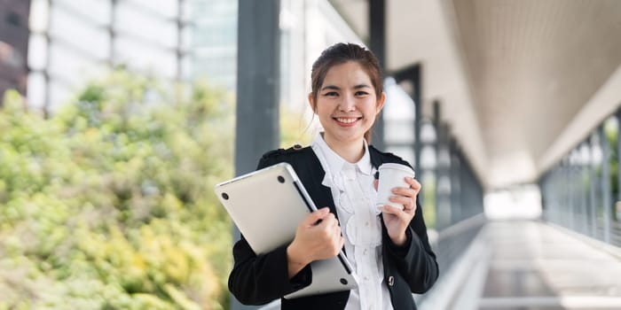 Young busy successful Asian business woman, professional businesswoman holding laptop and using mobile standing or walking on urban business center.