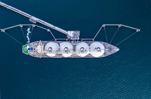 Aerial of Liquified Natural Gas LNG carrier moored to a small gas terminal. Fuel crisis. Sanctions. Top down shot.