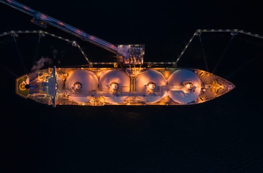 Aerial of Liquified Natural Gas LNG carrier moored to a small gas terminal at night. Fuel crisis. Sanctions. Top down shot.