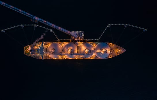 Aerial of Liquified Natural Gas LNG carrier moored to a small gas terminal at night. Fuel crisis. Sanctions. Top down shot.