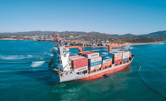 Aerial view of a RISE SHINE container cargo ship stands aground after a storm with floating boom around the ship to prevent the spread of petroleum. Container ship ran aground during the storm.