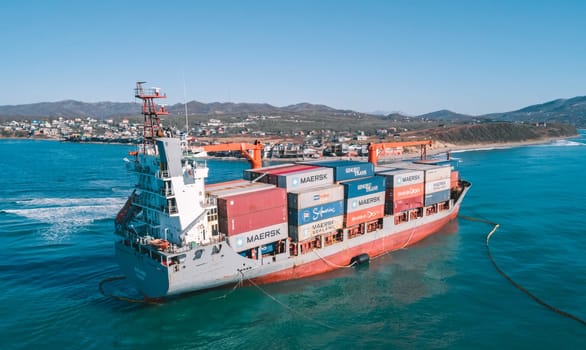 Aerial view of a RISE SHINE container cargo ship stands aground after a storm with floating boom around the ship to prevent the spread of petroleum. Container ship ran aground during the storm.