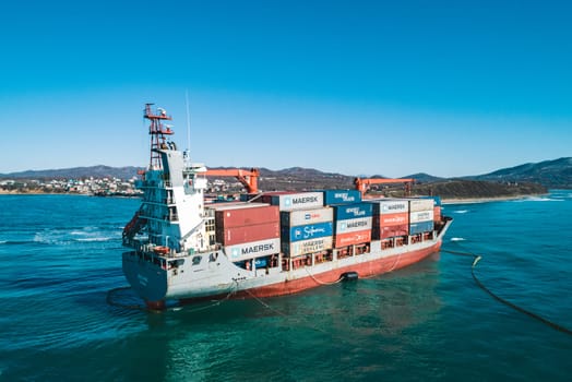 Aerial view of a RISE SHINE container cargo ship stands aground after a storm with floating boom around the ship to prevent the spread of petroleum. Container ship ran aground during the storm.