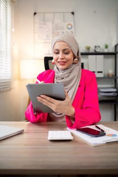 Young Muslim business woman hijab happy using digital tablet in modern office.