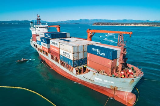 Aerial view of a RISE SHINE container cargo ship stands aground after a storm with floating boom around the ship to prevent the spread of petroleum. Container ship ran aground during the storm.