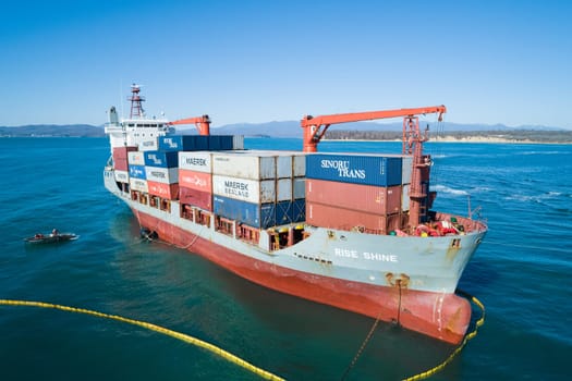 Aerial view of a RISE SHINE container cargo ship stands aground after a storm with floating boom around the ship to prevent the spread of petroleum. Container ship ran aground during the storm.