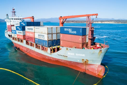 Aerial view of a RISE SHINE container cargo ship stands aground after a storm with floating boom around the ship to prevent the spread of petroleum. Container ship ran aground during the storm.