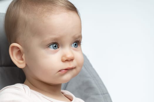 This close-up captures a baby’s thoughtful expression as they look to the side, not smiling but deeply engaged. It portrays the surprising depth of young minds, even at the tender age of one, reflecting on their surroundings with curiosity.
