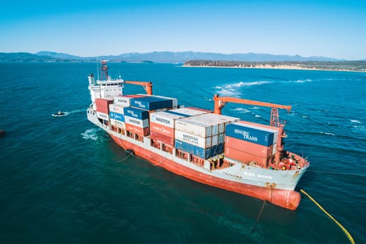 Aerial view of a RISE SHINE container cargo ship stands aground after a storm with floating boom around the ship to prevent the spread of petroleum. Container ship ran aground during the storm.