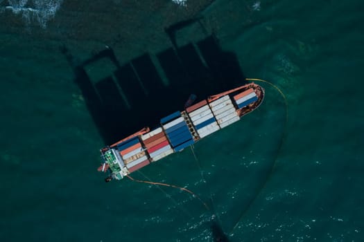 Aerial top down view of a container cargo ship stands aground after a storm with floating boom around the ship to prevent the spread of petroleum..