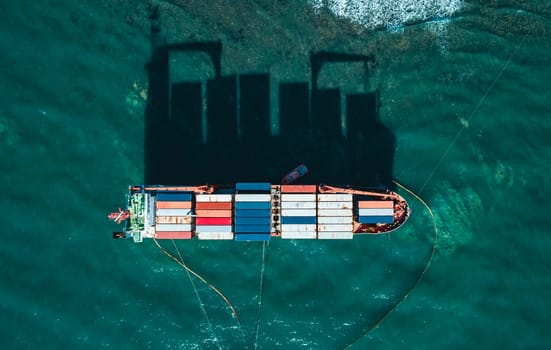 Aerial top down view of a container cargo ship stands aground after a storm with floating boom around the ship to prevent the spread of petroleum..